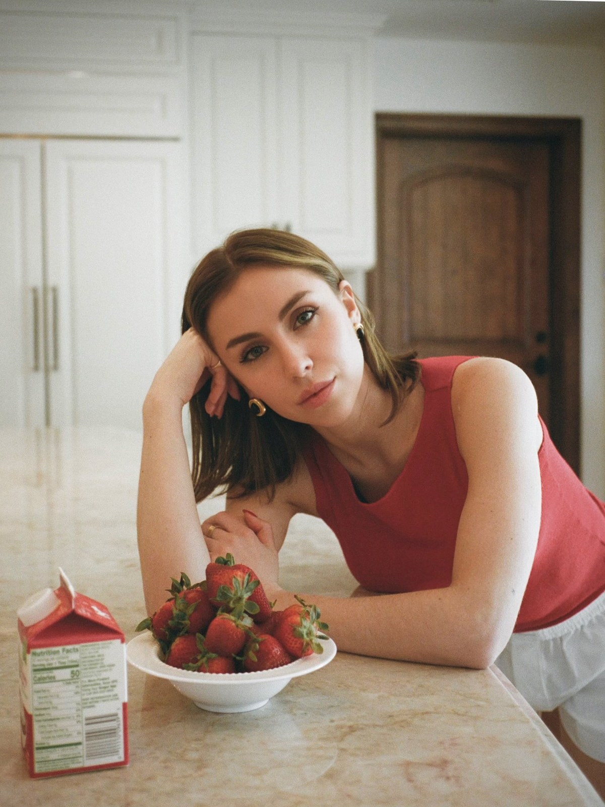 Woman in a coral sleeveless top leaning at a kitchen counter