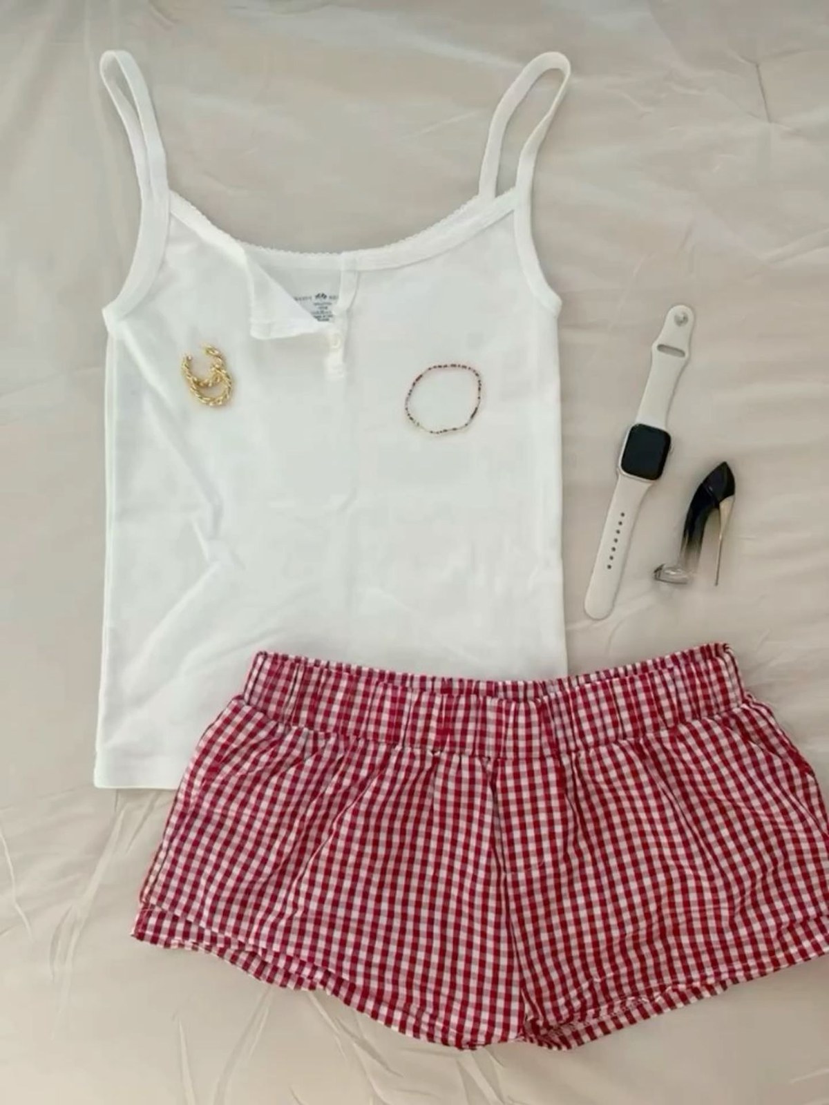 A white tank and red gingham shorts laid out with a watch and bracelet