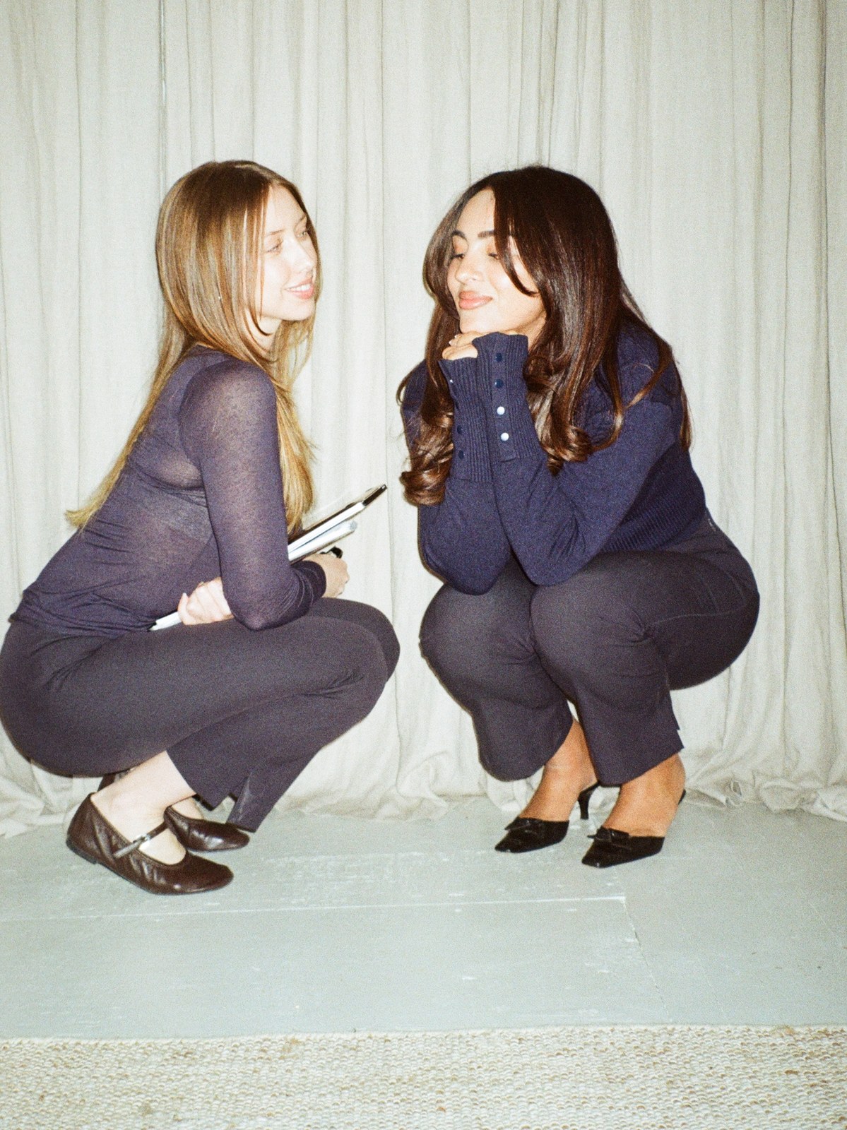 Two women in dark clothes seated together in a softly lit room