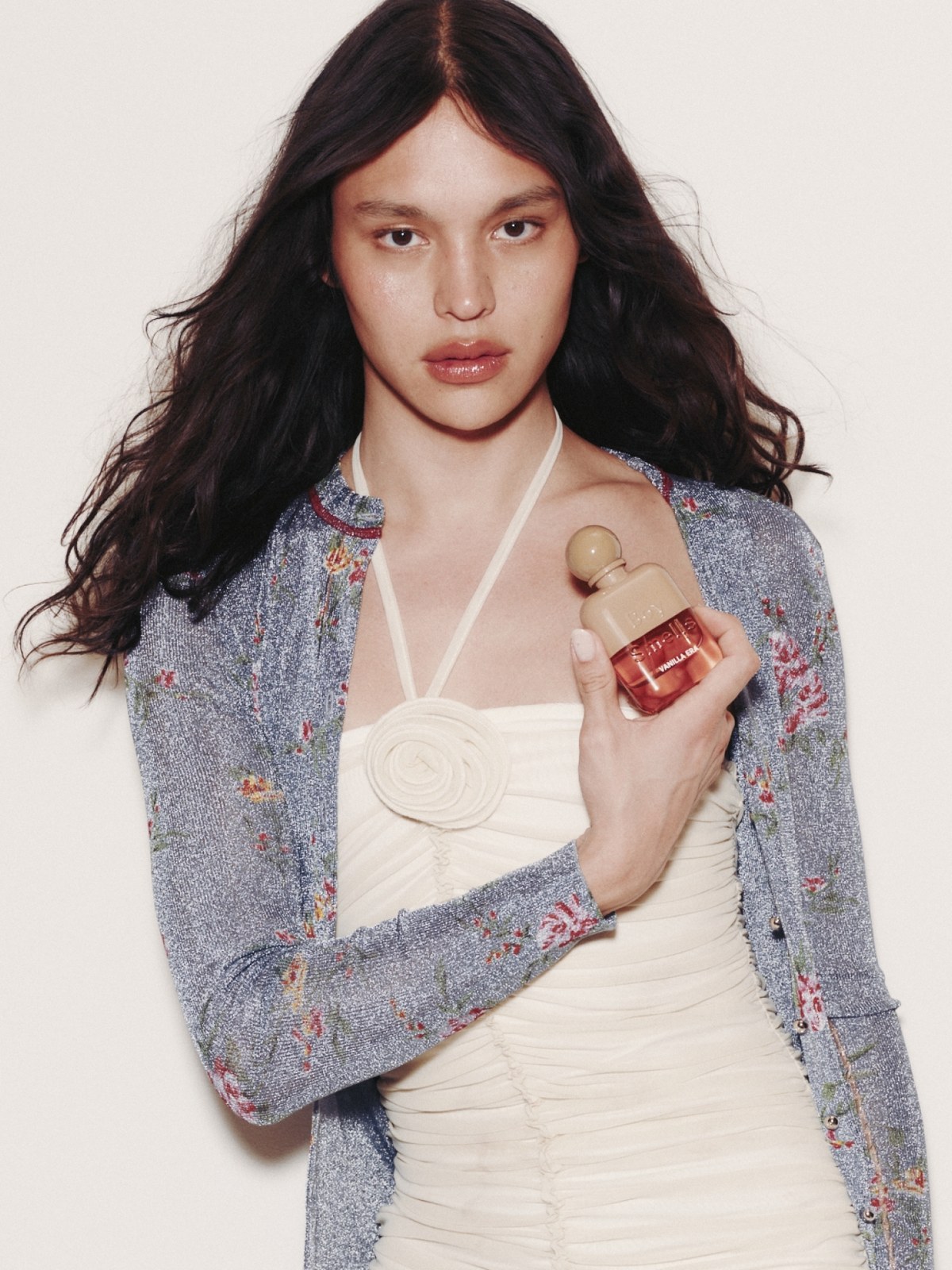Model in a light floral jacket holding a Boy Smells fragrance bottle