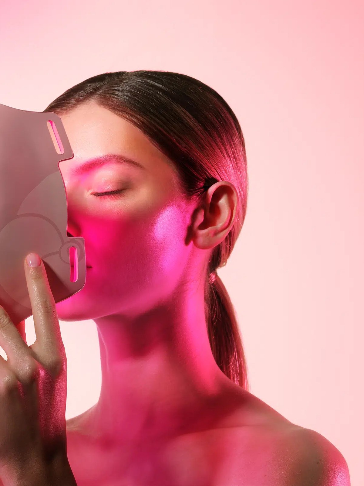 Model using a pink LED facial mask in a pink-lit studio