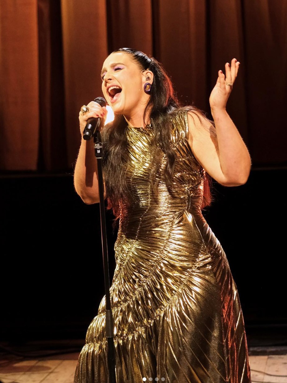 Jessie Ware performing in a gold pleated dress