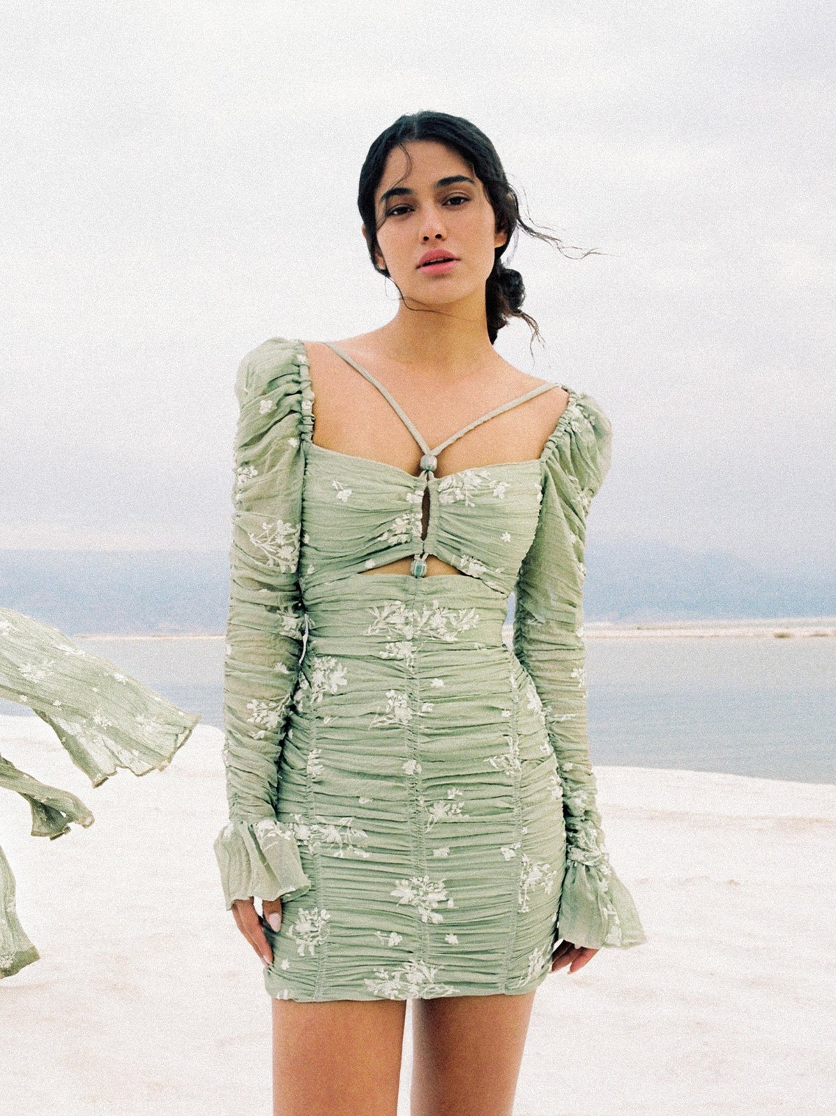 Model in a pale green embroidered dress against a waterside landscape