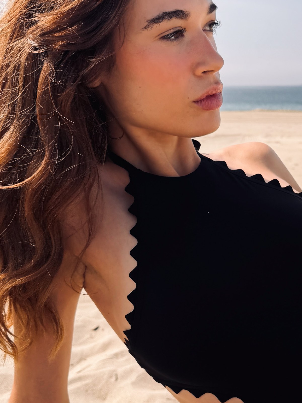 Model on the beach in a black scalloped edge halter one piece