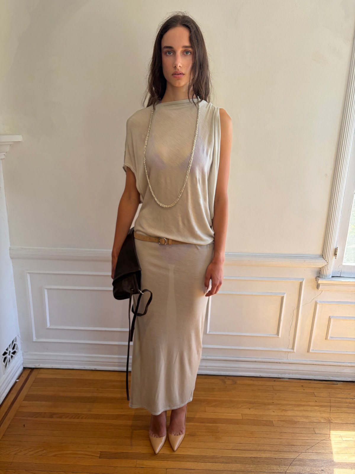 Model wearing a pale champagne top and neutral skirt in a room with a patterned wall
