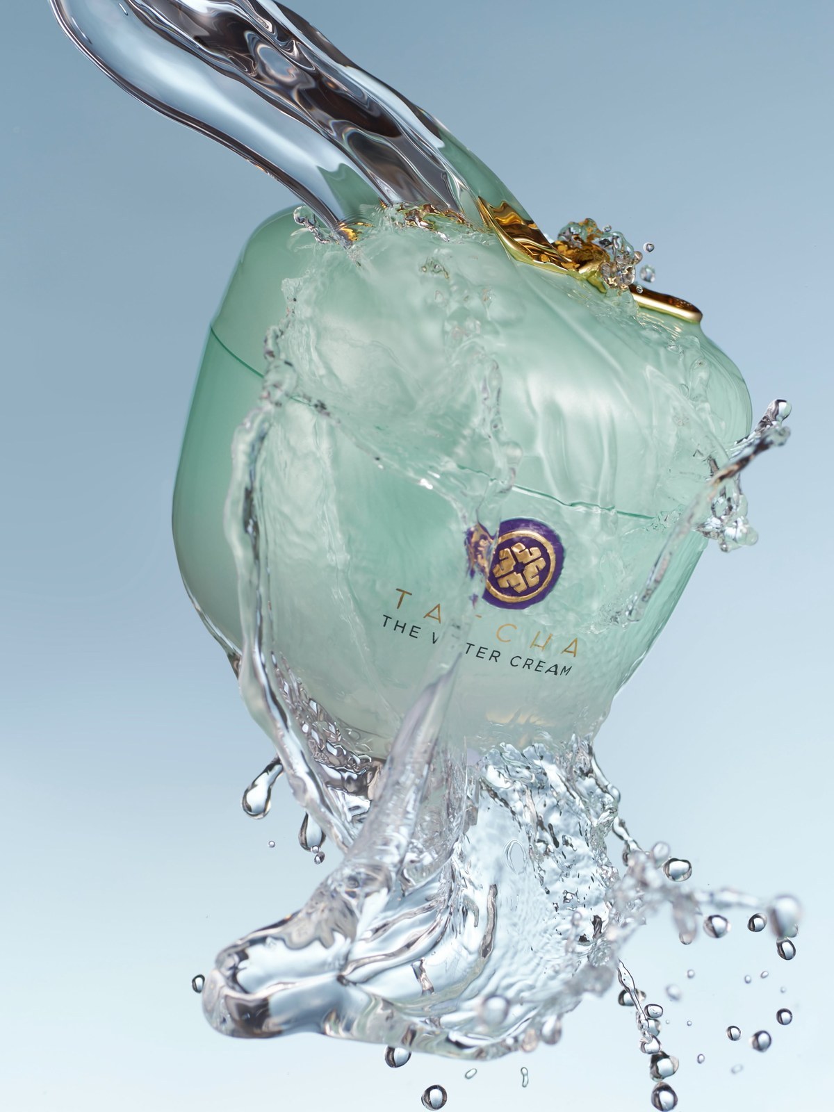 Pale green Tatcha The Water Cream jar surrounded by a splash of water against a blue background