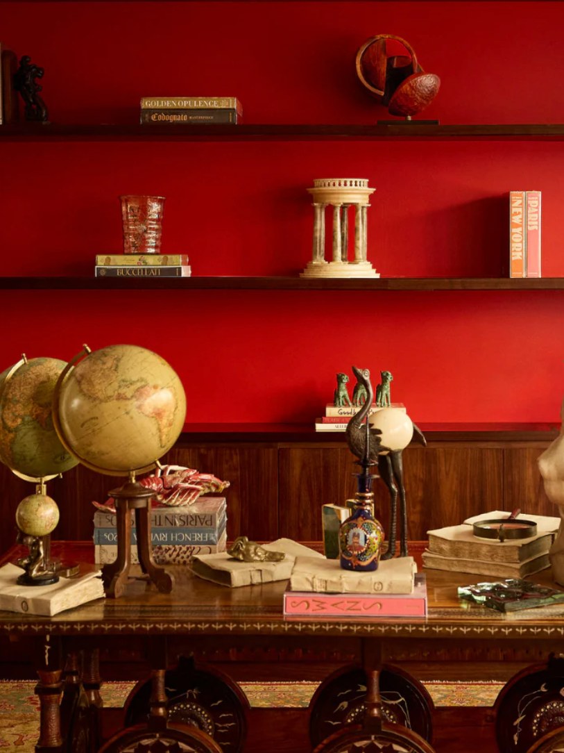 A warm red library vignette with antique objects and books.