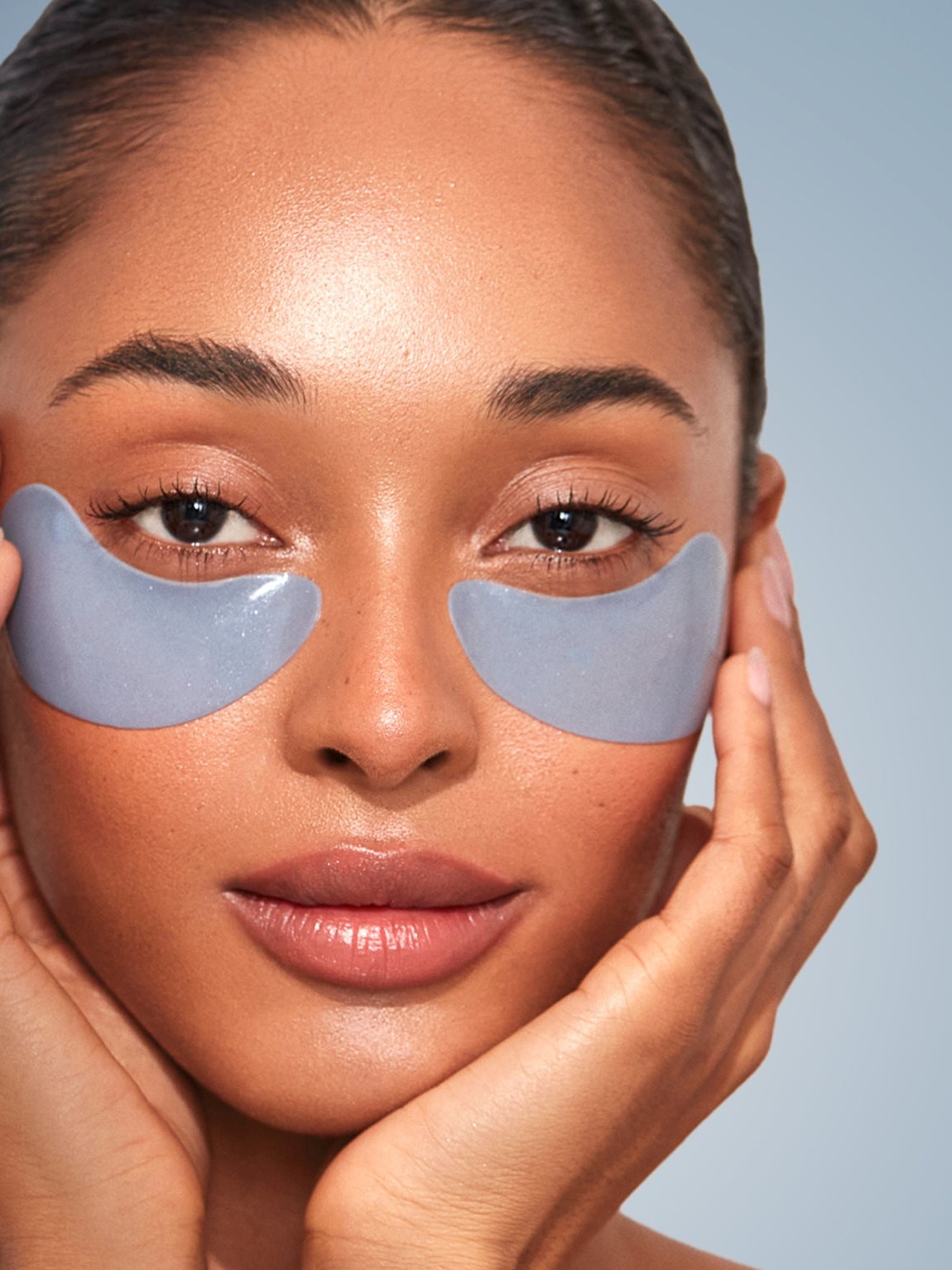 Model touching blue under-eye masks in a close beauty portrait
