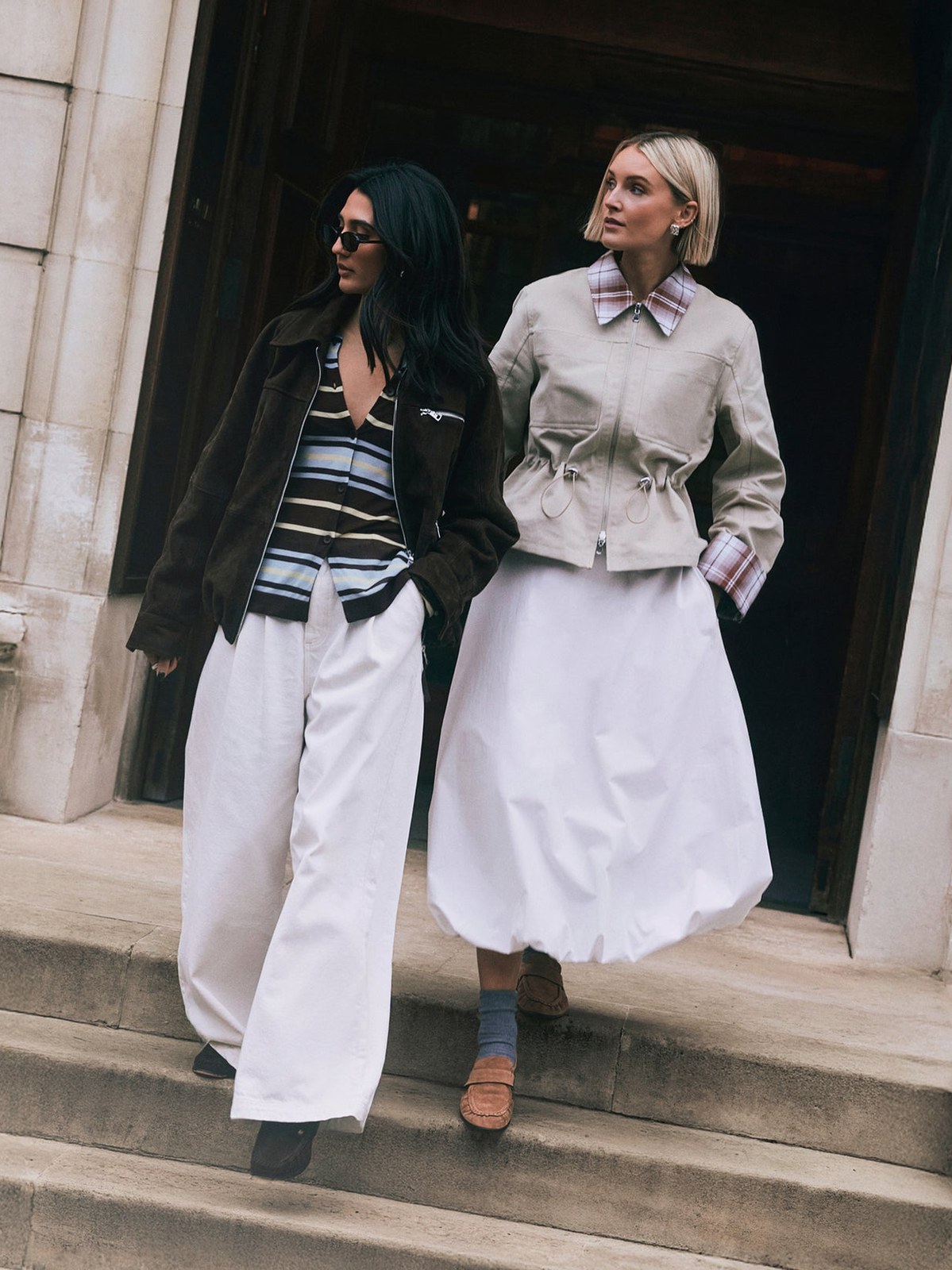 Two women in pale jackets and skirts walking on city steps for ALIGNE’s SS26 campaign