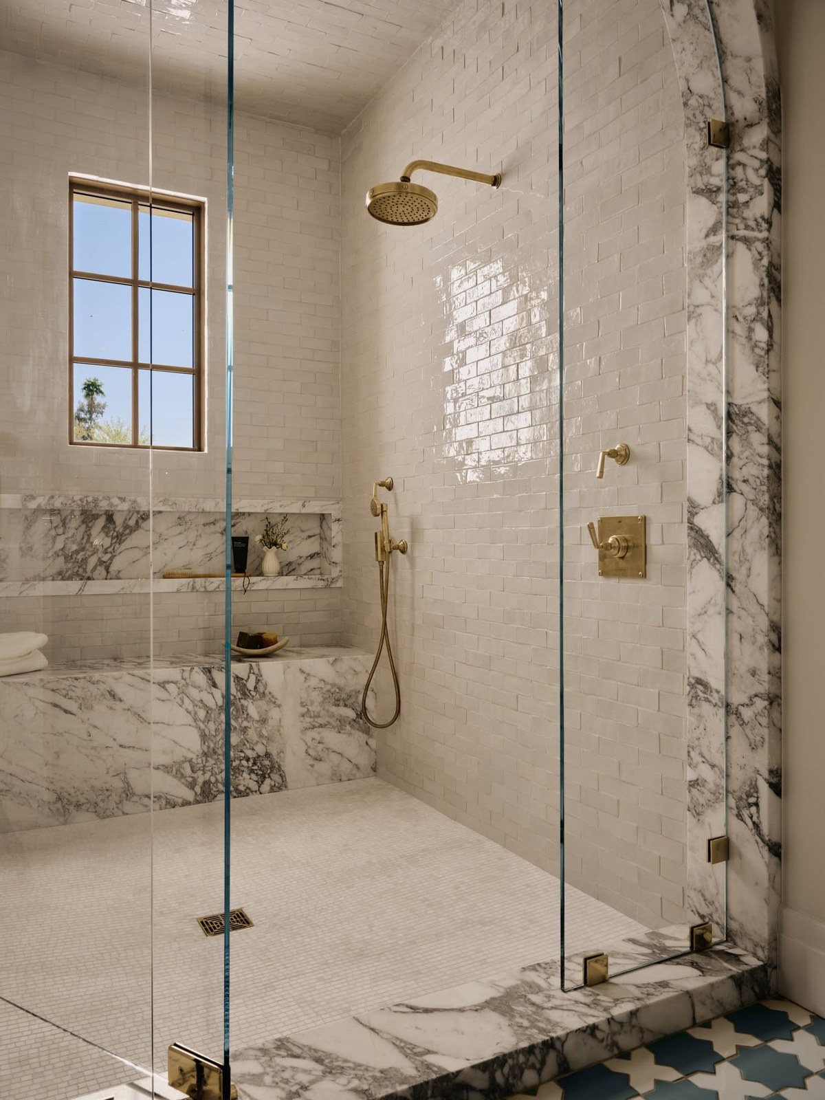 Glass-walled shower with marble tile and a window