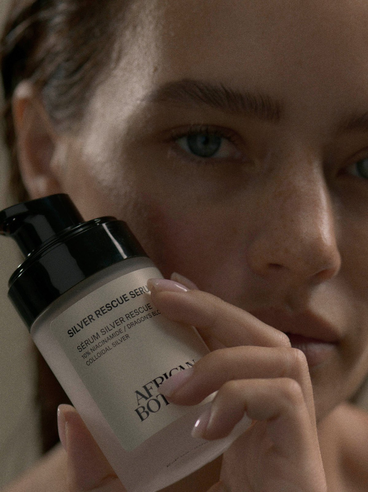 Close portrait of a model holding a skincare bottle near her cheek