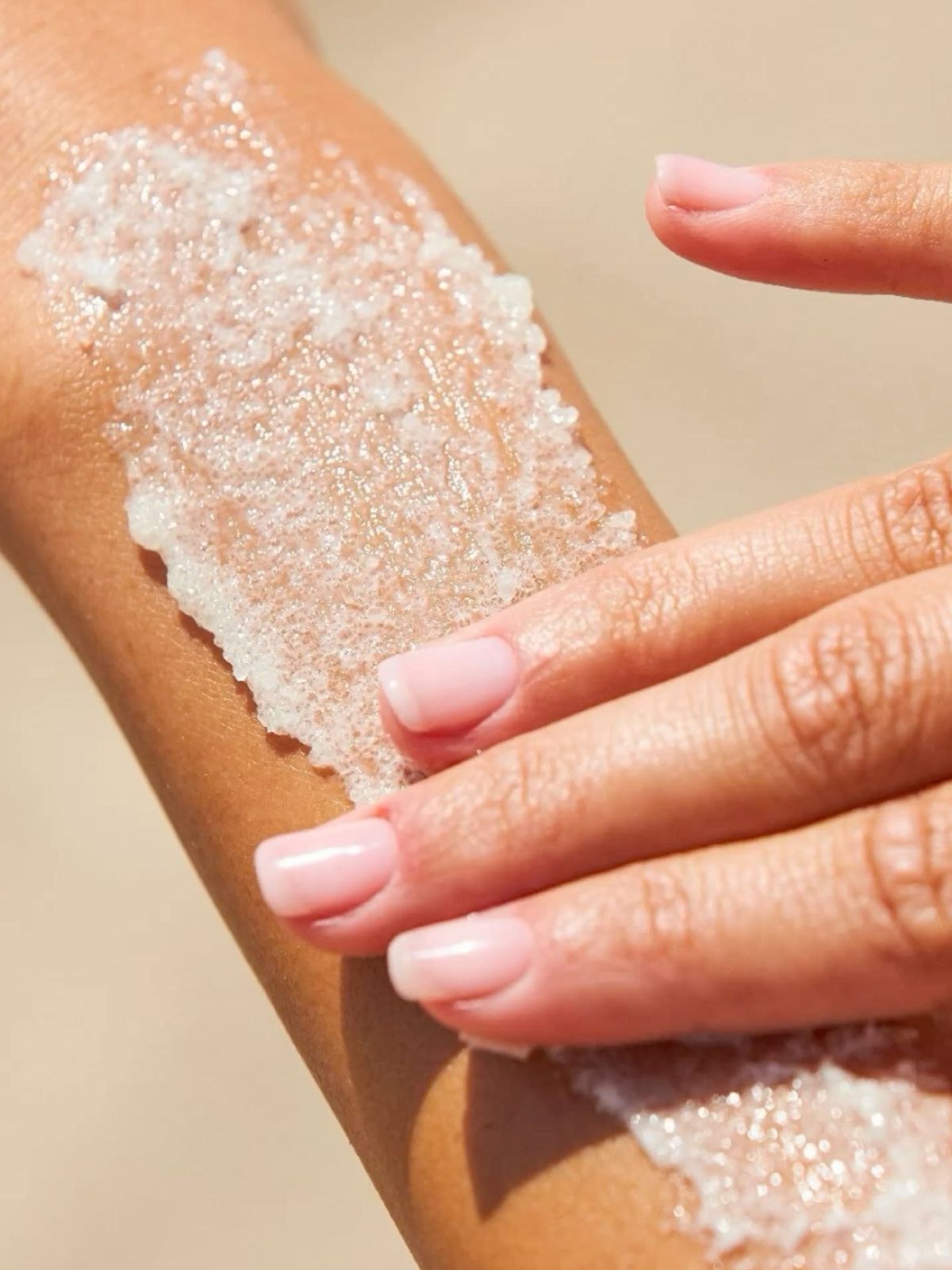 Close-up of a white sugar scrub spread across a forearm as fingers rub it in