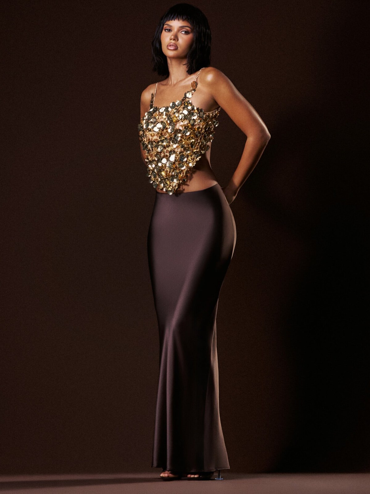 Model in a gold embellished top and dark fitted skirt against a studio backdrop