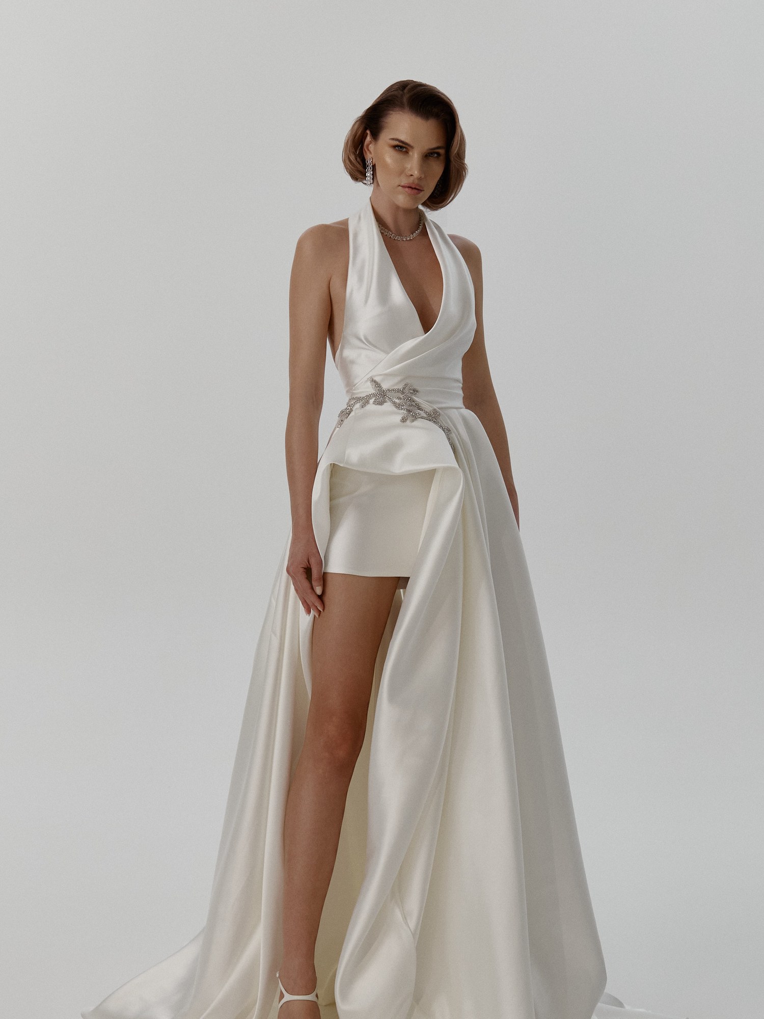Model in a white satin halter mini dress with a draped overskirt and crystal belt