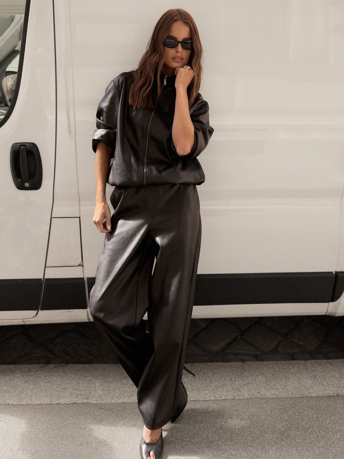 Model in a black leather-look outfit beside a white van