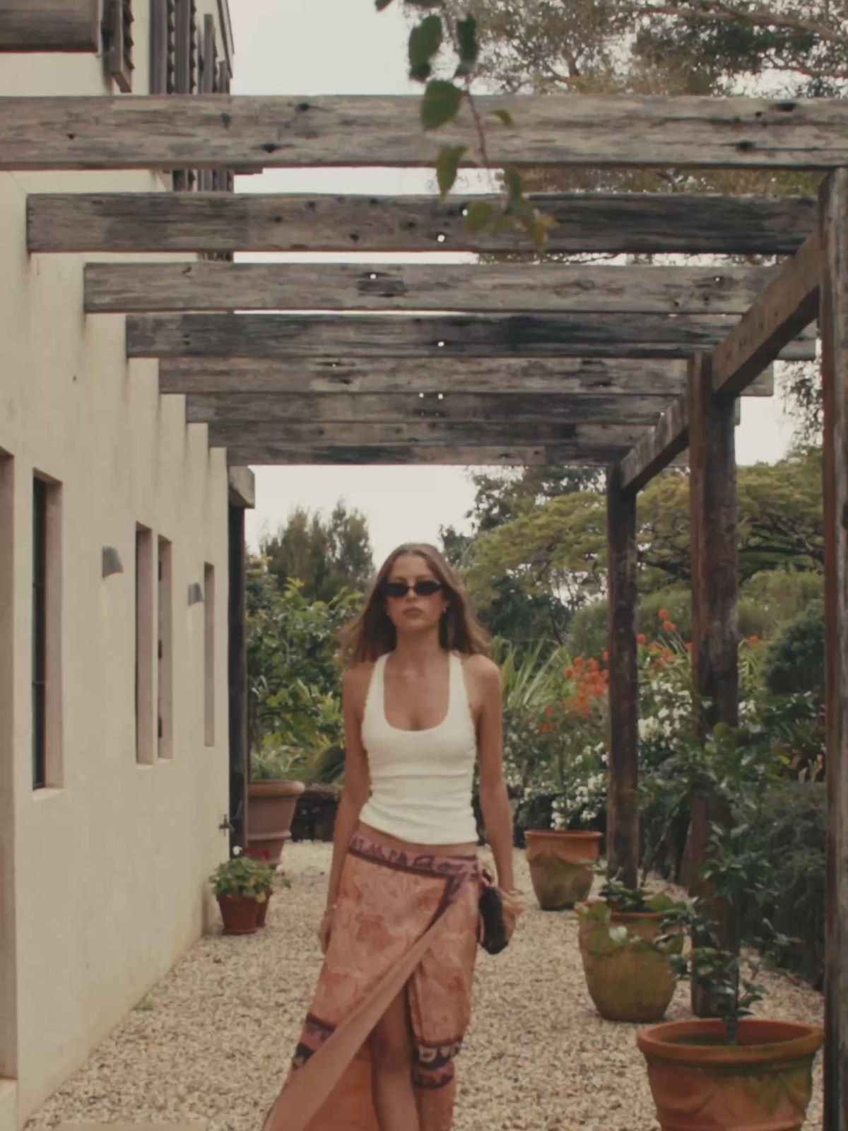 Model in a white tank and patterned pink maxi skirt walking through a courtyard