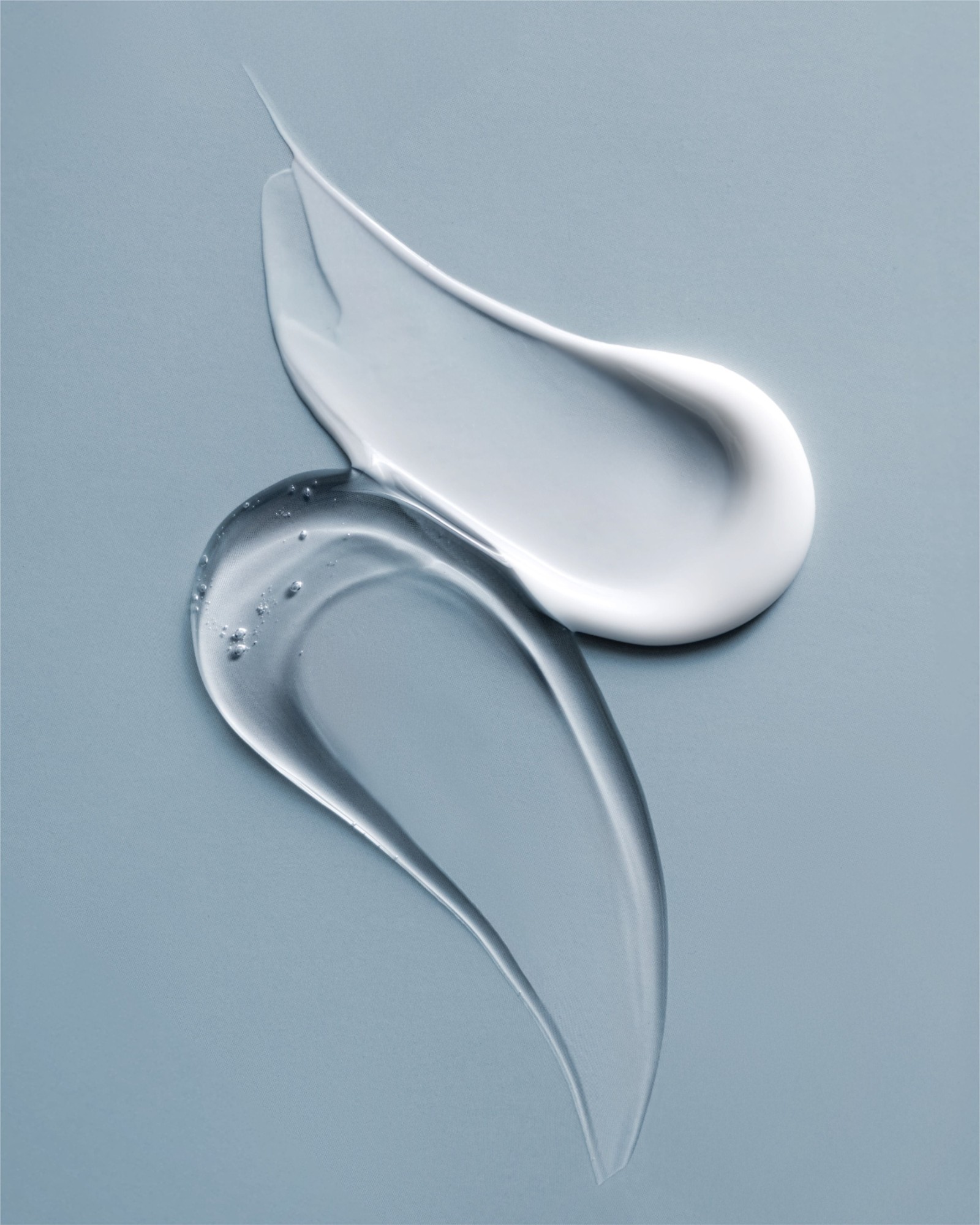 Swatches of white cream and clear gel on a pale blue-grey background