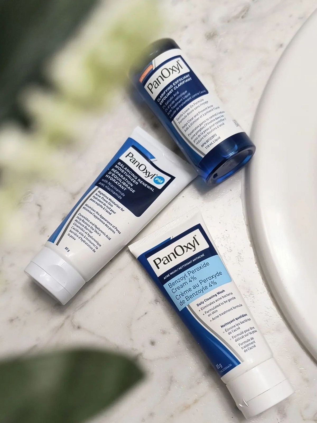 PanOxyl clarifying exfoliant, moisturizer and cream tubes laid out on a marble counter