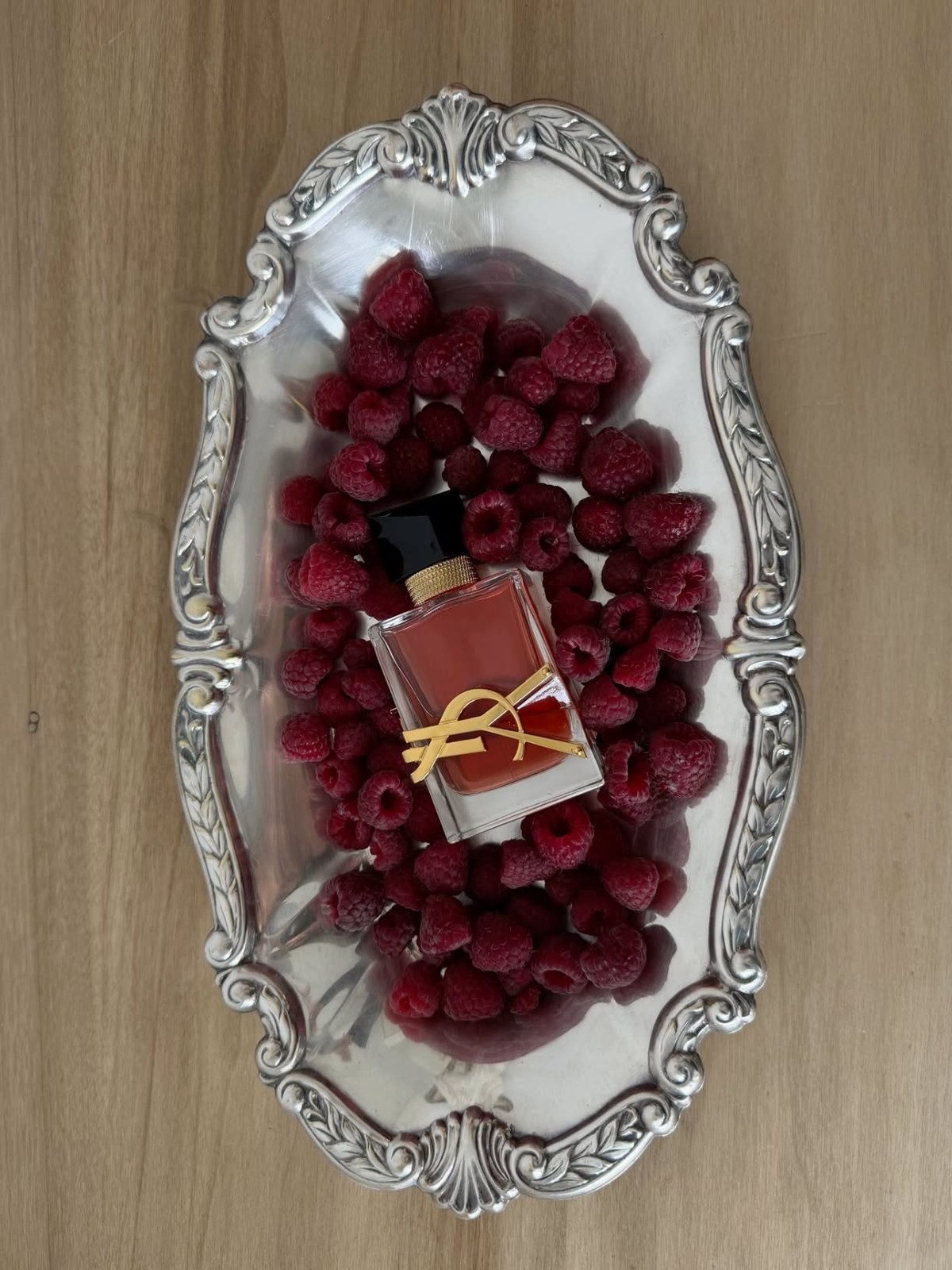 Small YSL perfume bottle nestled in fresh raspberries on a silver tray