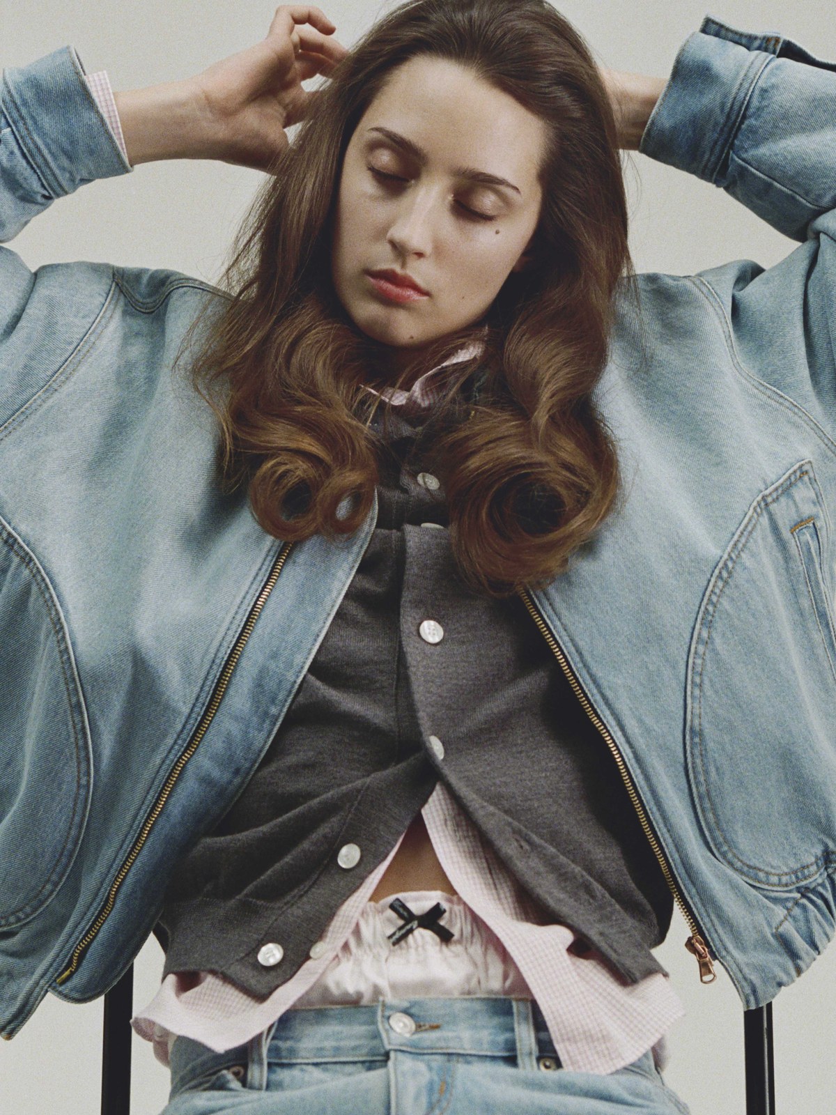 Model in a pale denim jacket and charcoal top seated in a studio