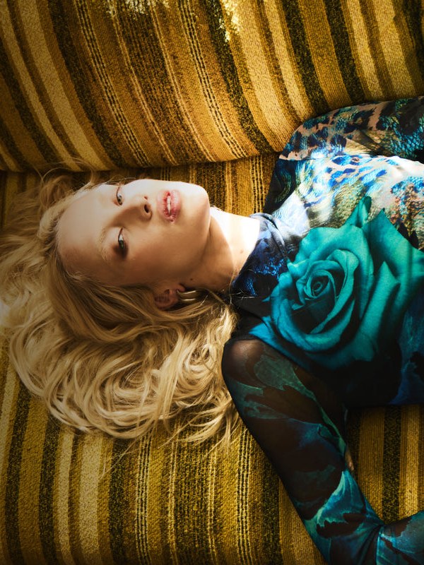 Blonde model reclining in an AFRM blue floral look against gold striped upholstery