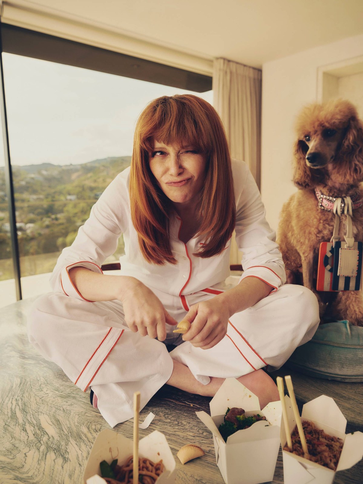 Natasha Lyonne lounging in a cream striped set by a window