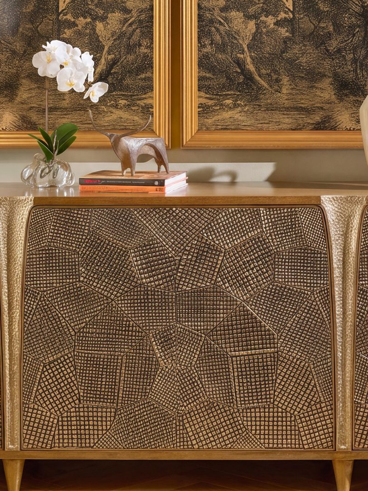 Carved gilt sideboard styled with framed landscapes, a lamp and vases between two chairs