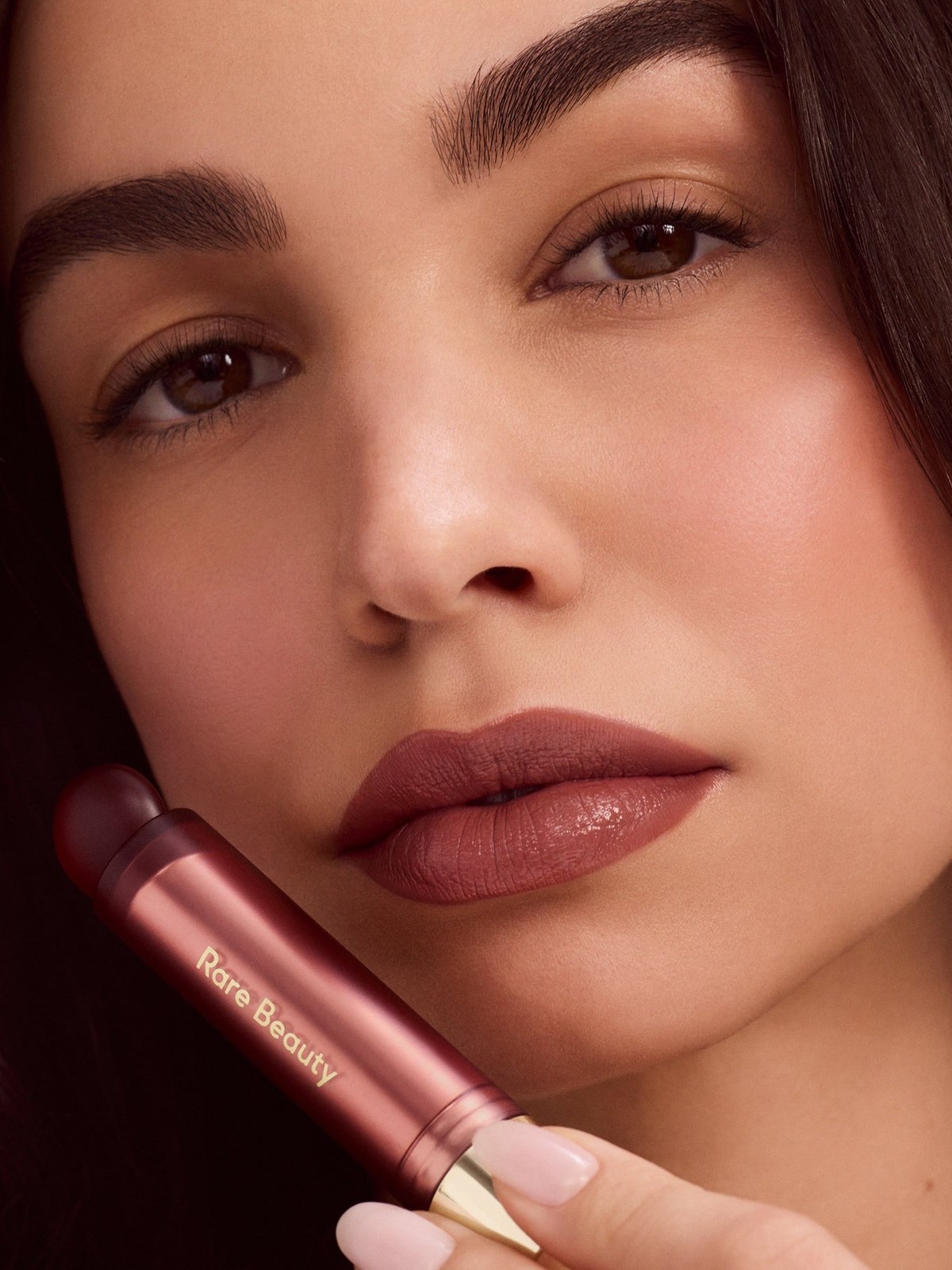 Close-up of a woman with a berry lip oil stick holding the tube