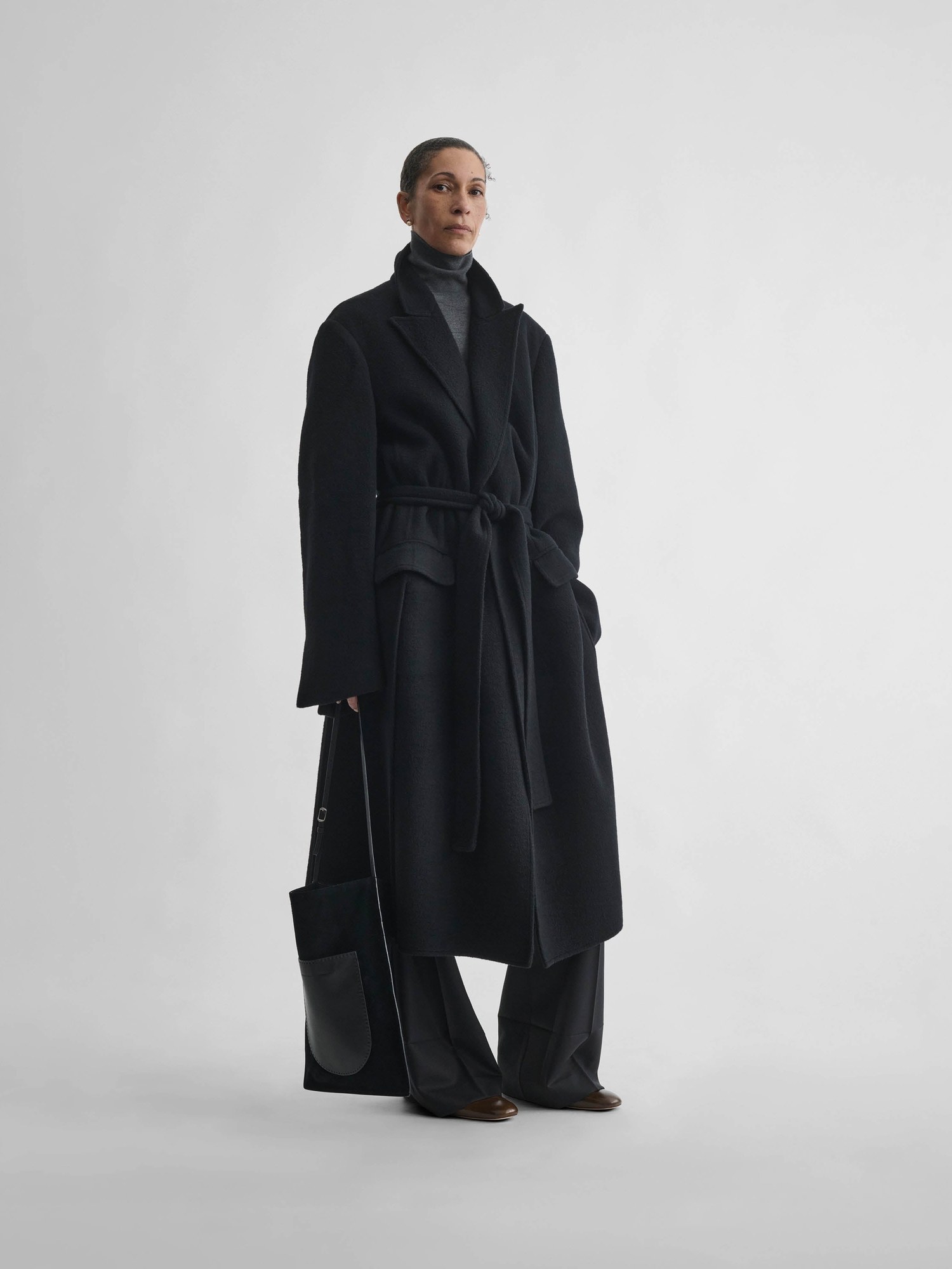 Model in a black cashmere belted robe coat holding a bag