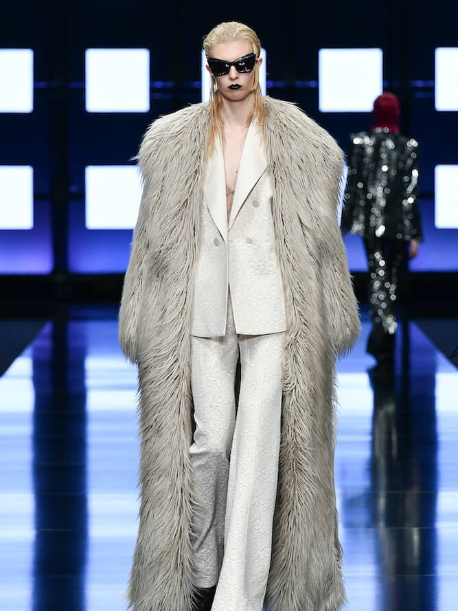 Runway model in a pale suit layered beneath a long textured coat