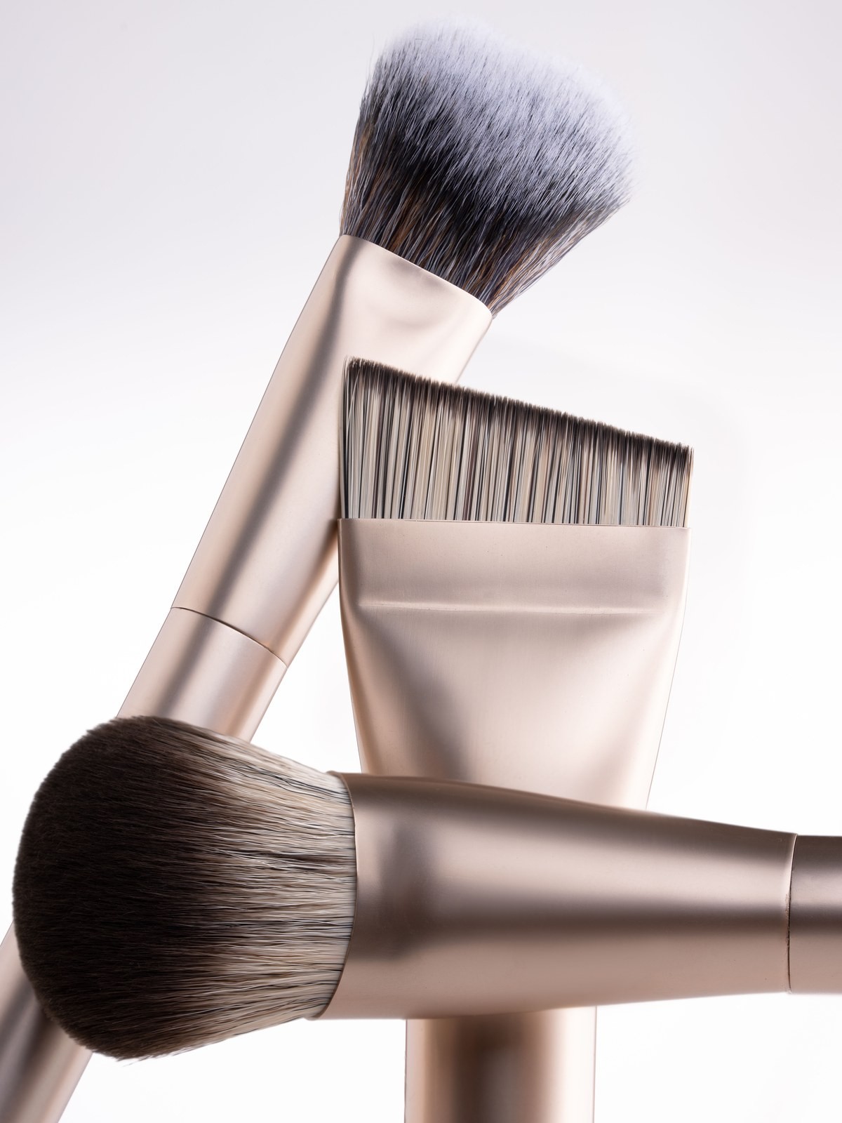 Close up of three makeup brushes with metallic gold handles crossed together