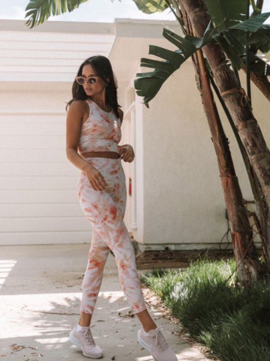 Model in a pink printed activewear set walking beside palm trees