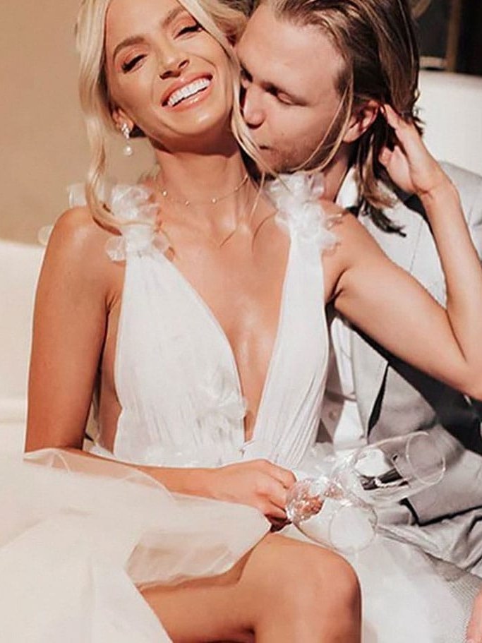 Bride in a ruffled white gown sharing a candid moment with her partner indoors