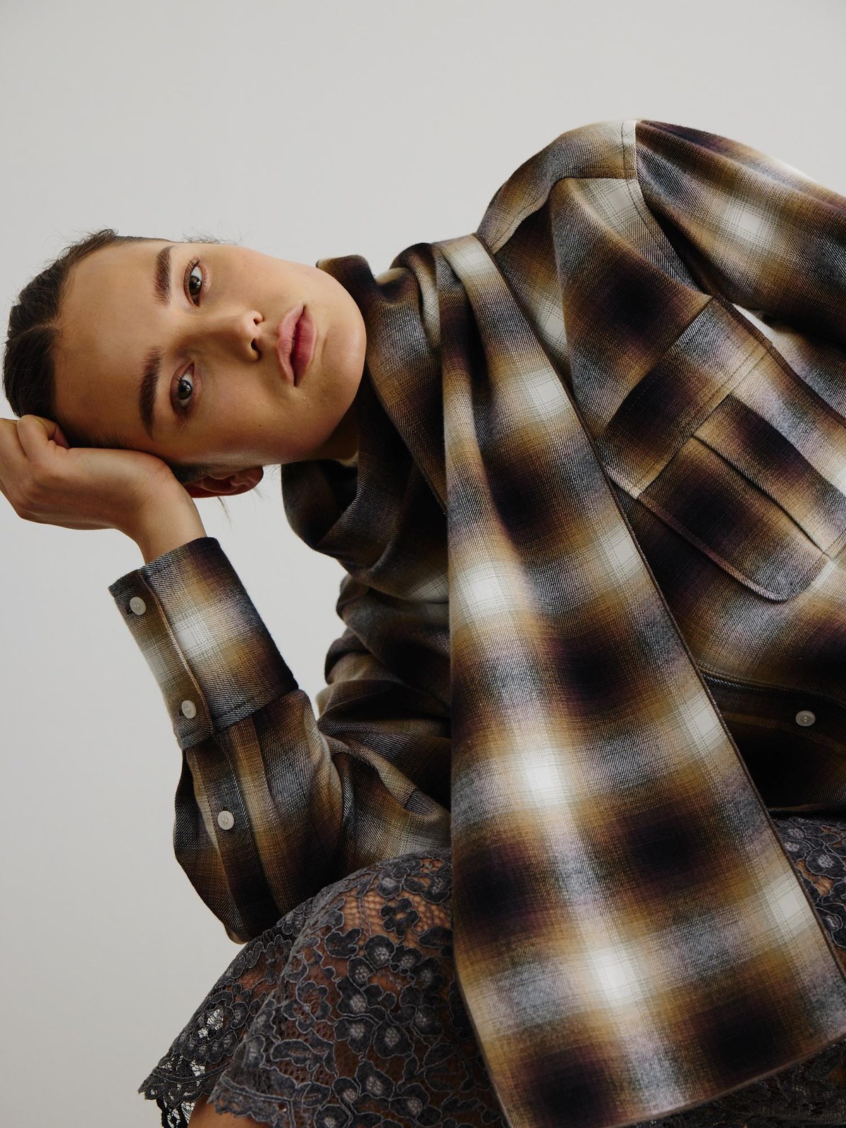 Model reclining in a plaid Smythe jacket and lace skirt