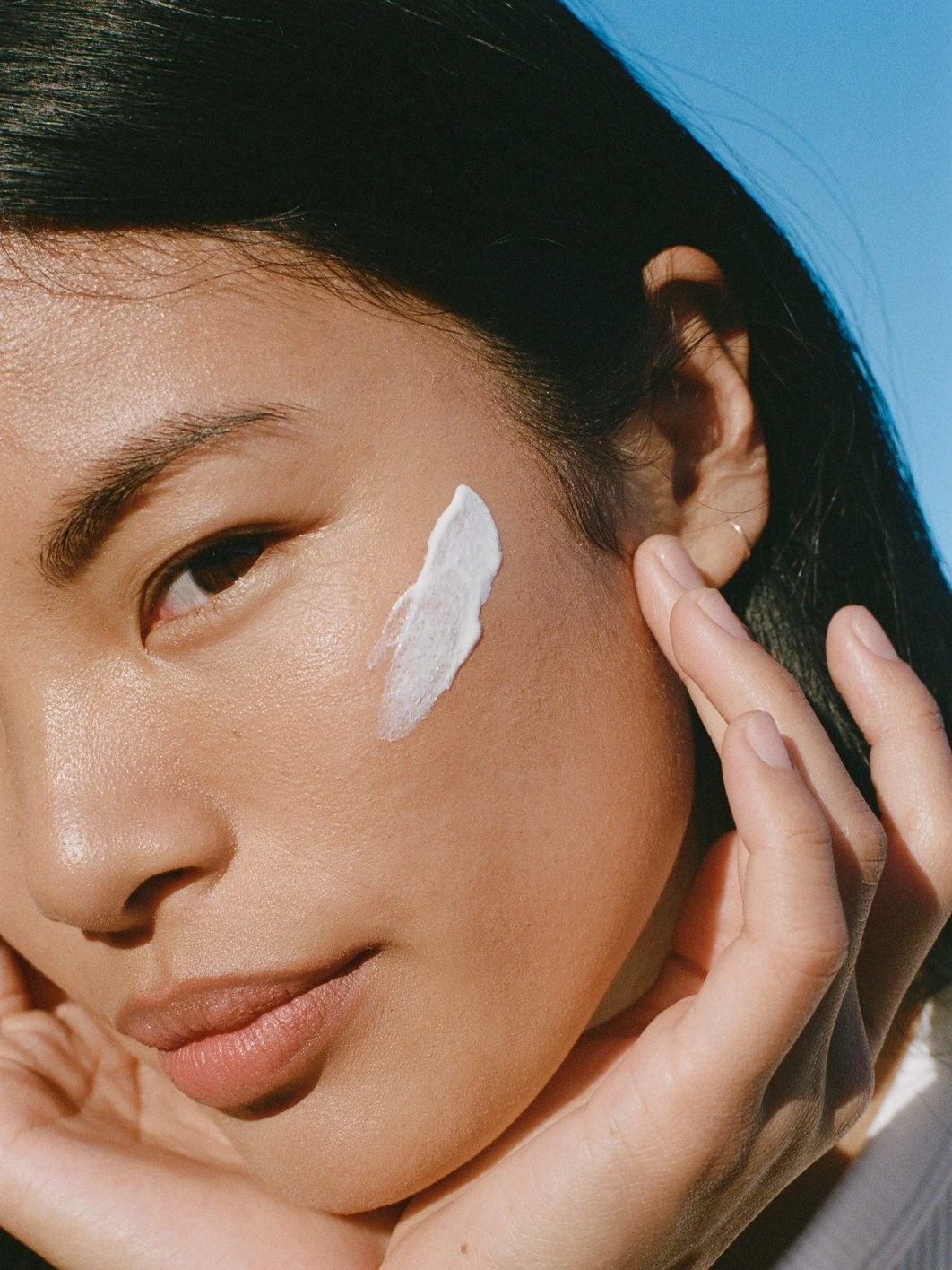 Close portrait of a woman applying cream to her cheek