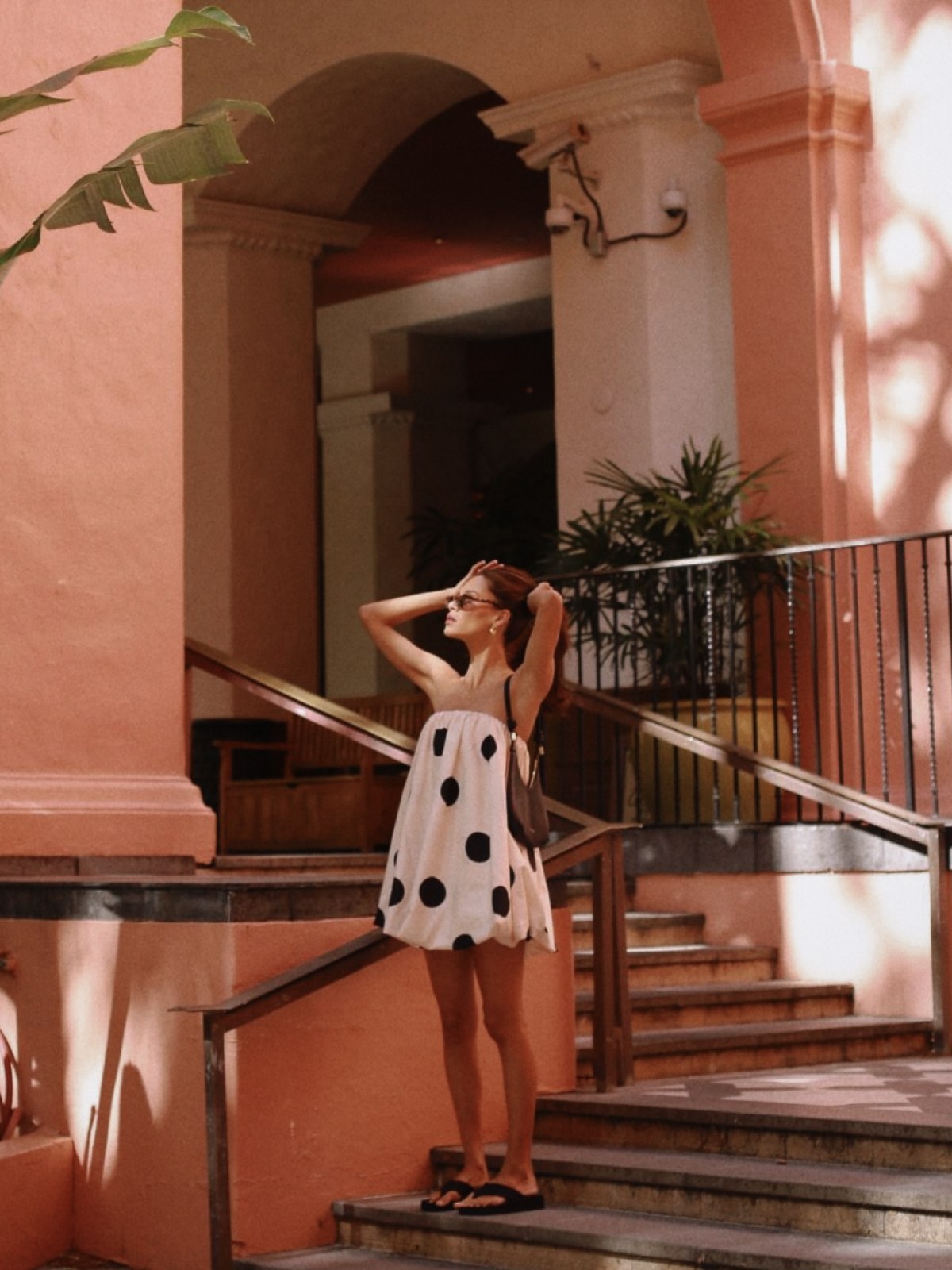 Model in a white spotted dress on pink courtyard steps