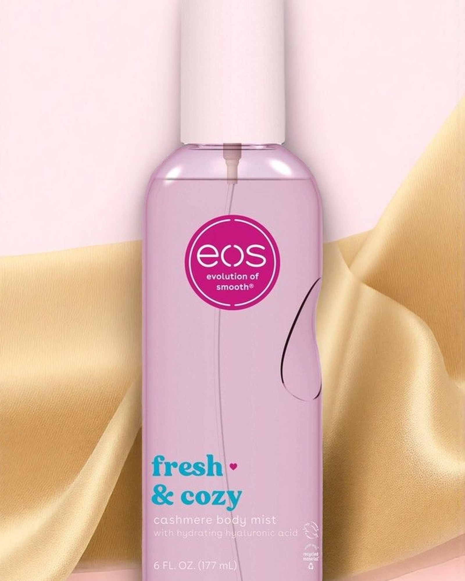 Pink eos Fresh & Cozy cashmere body mist bottle with a white cap in front of gold satin fabric on a pale pink background
