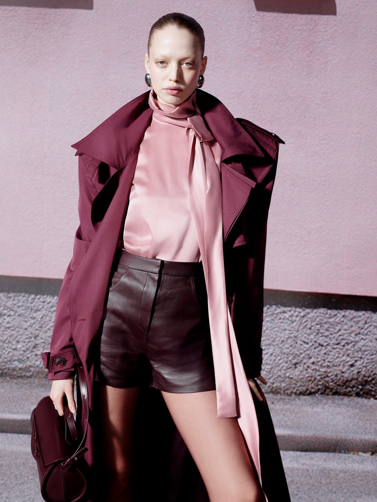 Model in a mauve coat and dark shorts on a city sidewalk