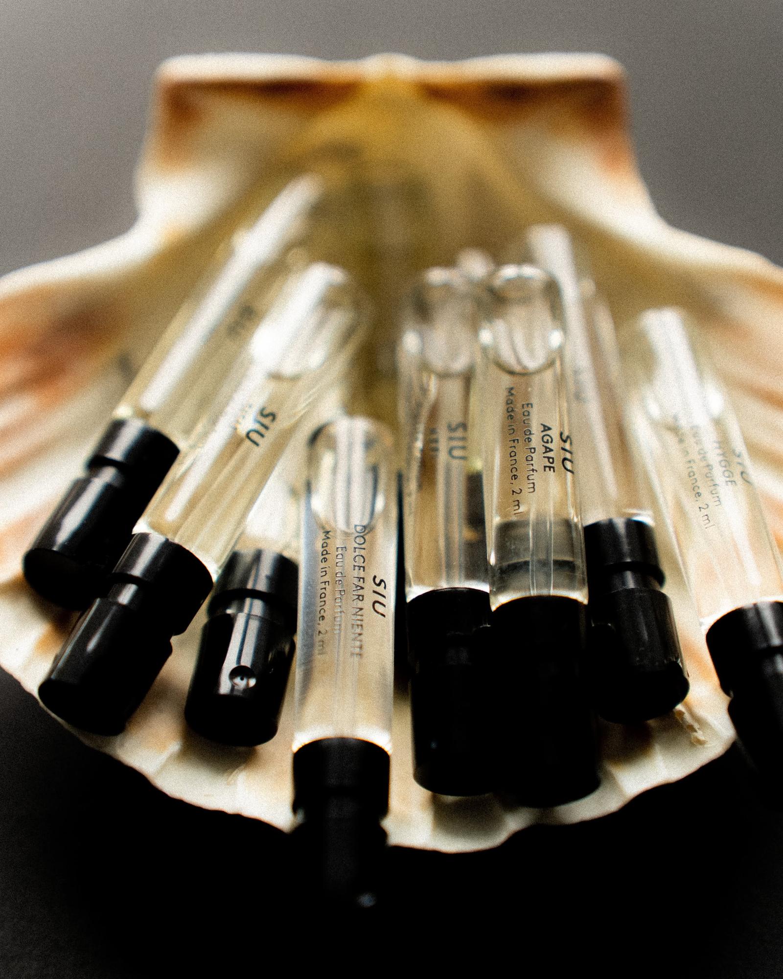 A cluster of tiny two milliliter eau de parfum sample vials with black caps resting in a scallop shell