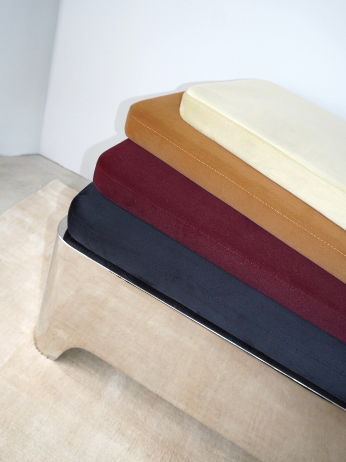 Stacked bench cushions in cream, ochre, burgundy and navy over a pale rug