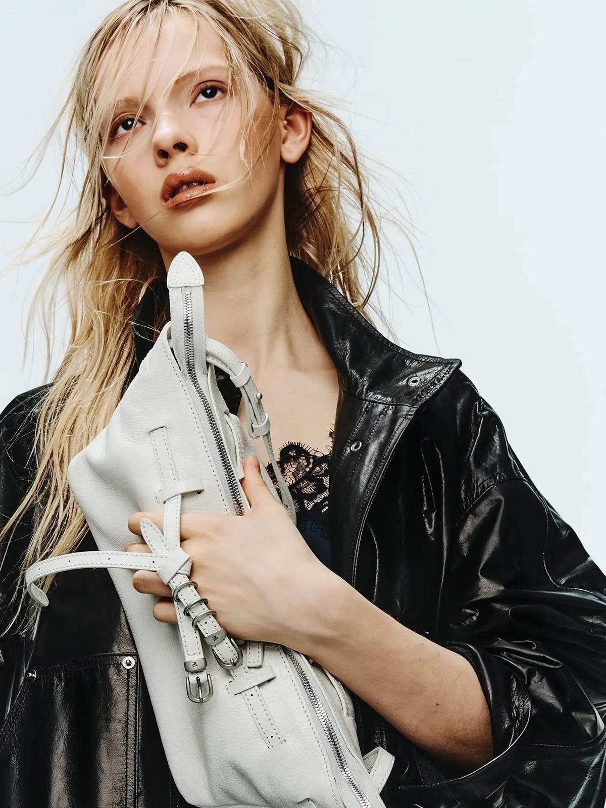 Model in a leather jacket holding a white MARGESHERWOOD bag in a studio