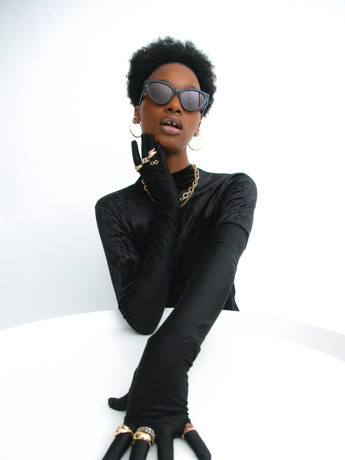 Model in dark Lexxola sunglasses and a black outfit against a pale studio background