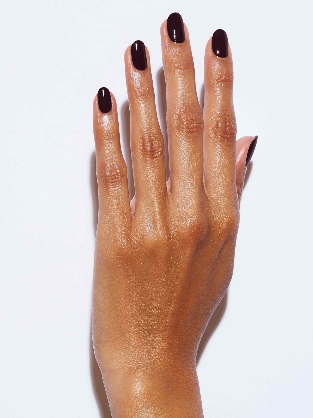 Close up of a hand with glossy dark burgundy short gel nails against a white background