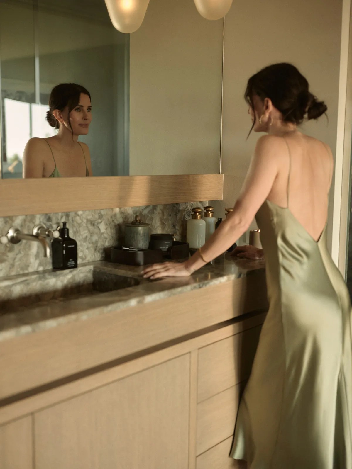 Courteney Cox reflected in a bathroom mirror beside Homecourt products