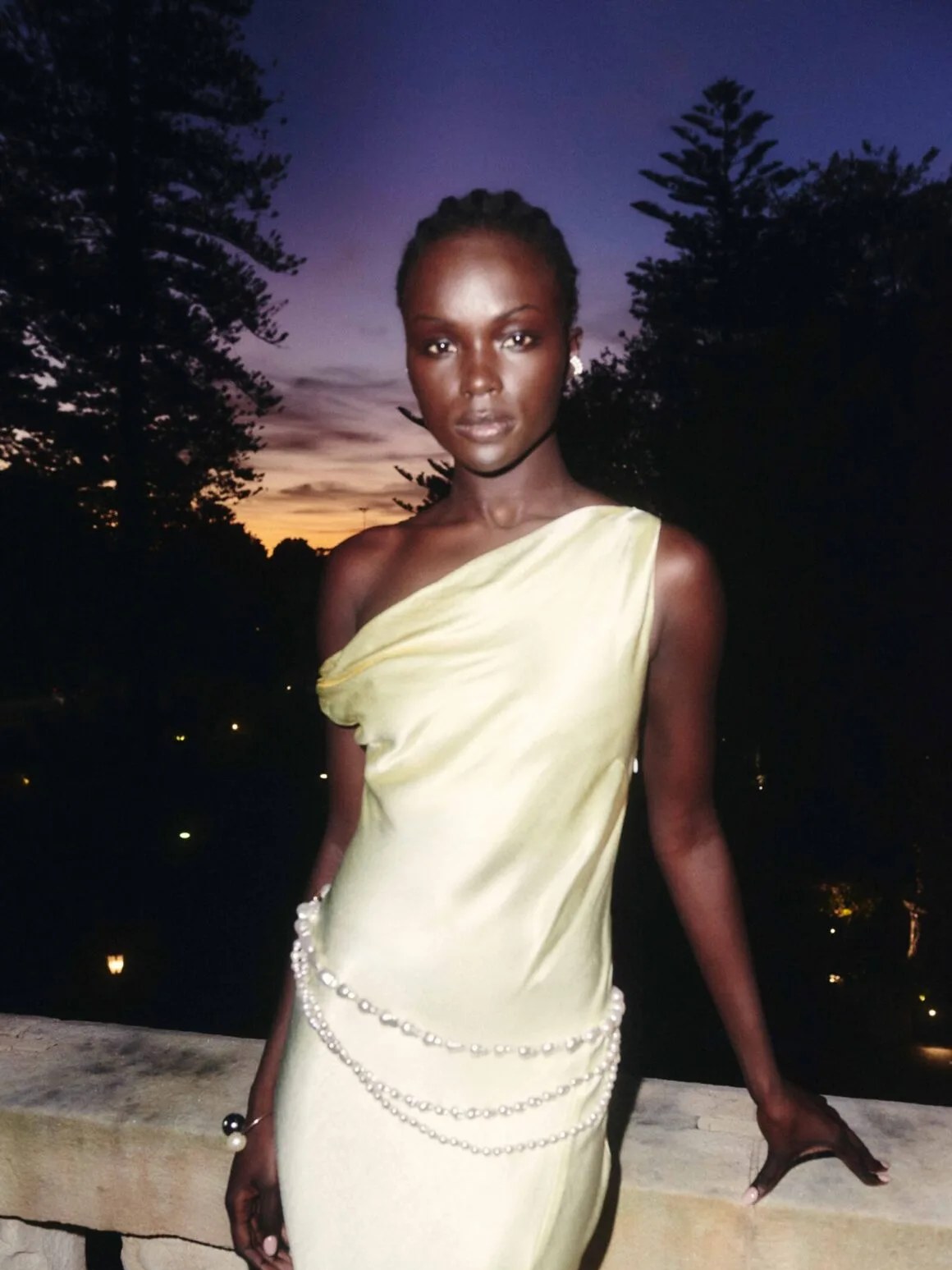 Model wearing a pale yellow evening dress outdoors at dusk