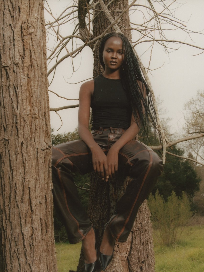 Model seated on a tree trunk in a dark sleeveless top and trousers