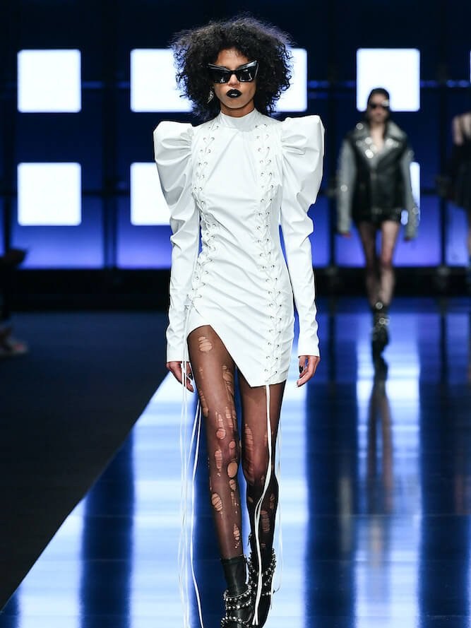 Runway model in a white ruffled mini dress and dark boots