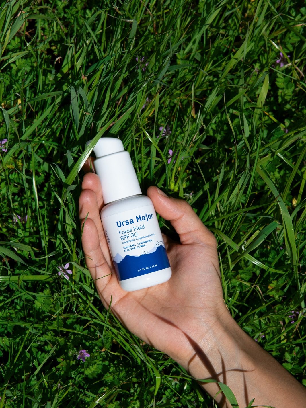 A hand holding Ursa Major face wash over green grass