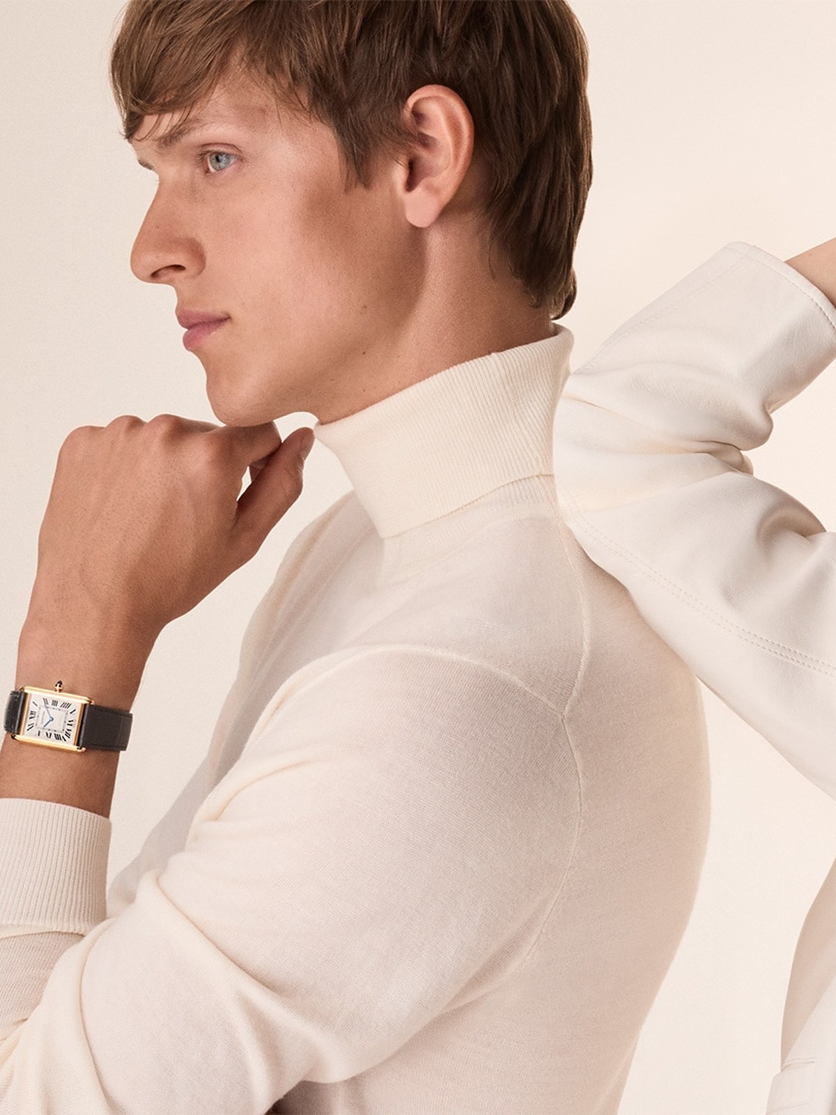 Man in a cream knit with a Tank watch and a model behind him