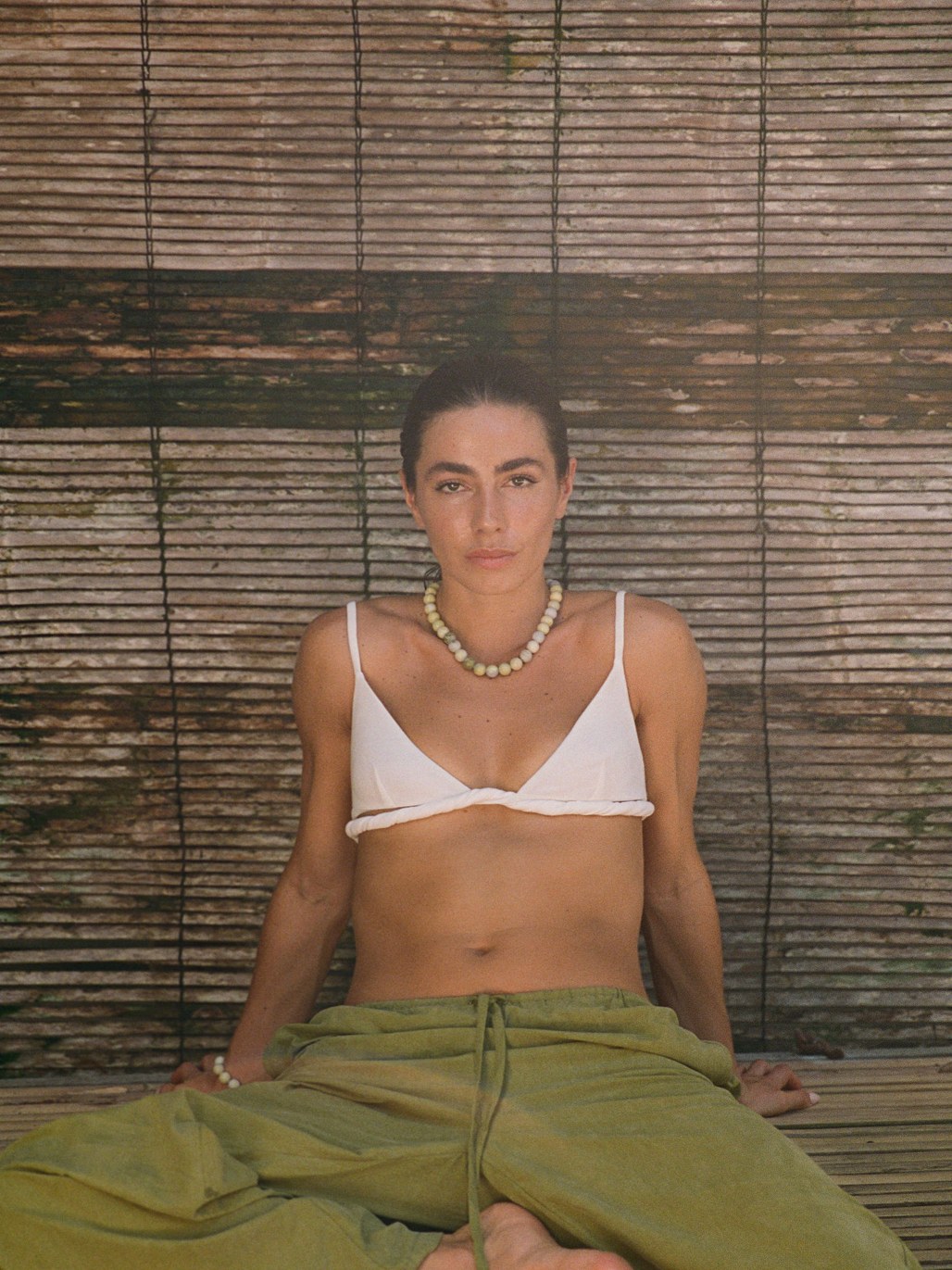 Model seated in a white top and green trousers wearing a beaded necklace